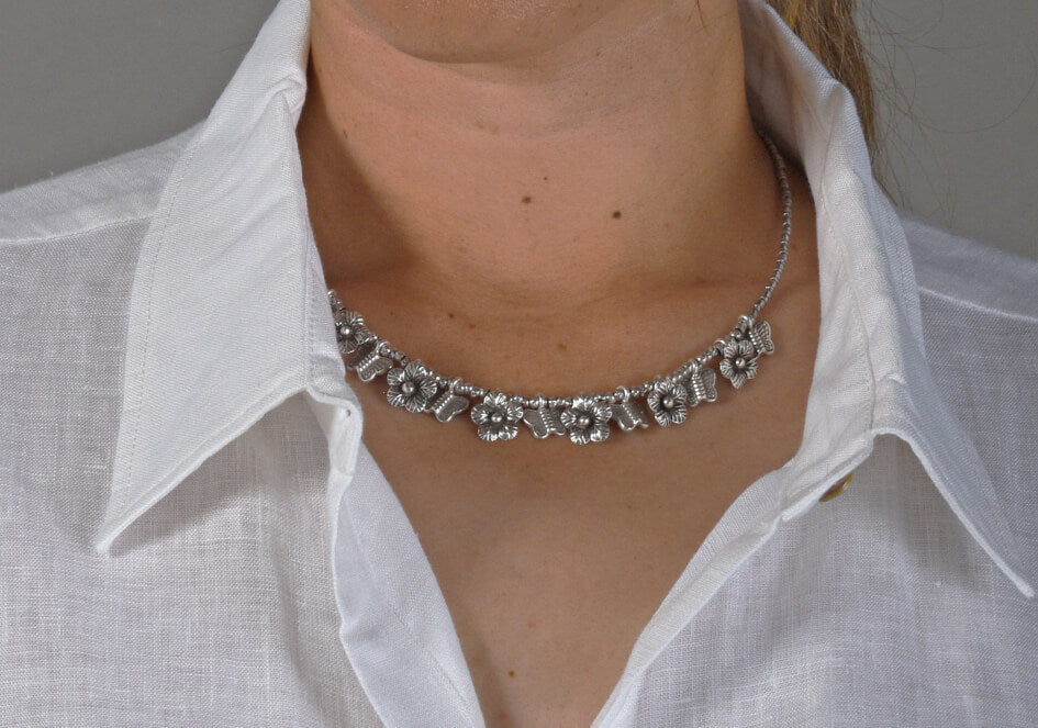Zoomed in photo of a model wearing a silver necklace with flower and butterfly silver charms