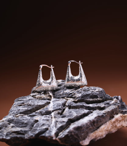 Naya Sterling Silver 925 hoop earrings with trapezoid shape and oxidised floral engravings, displayed on dark stone