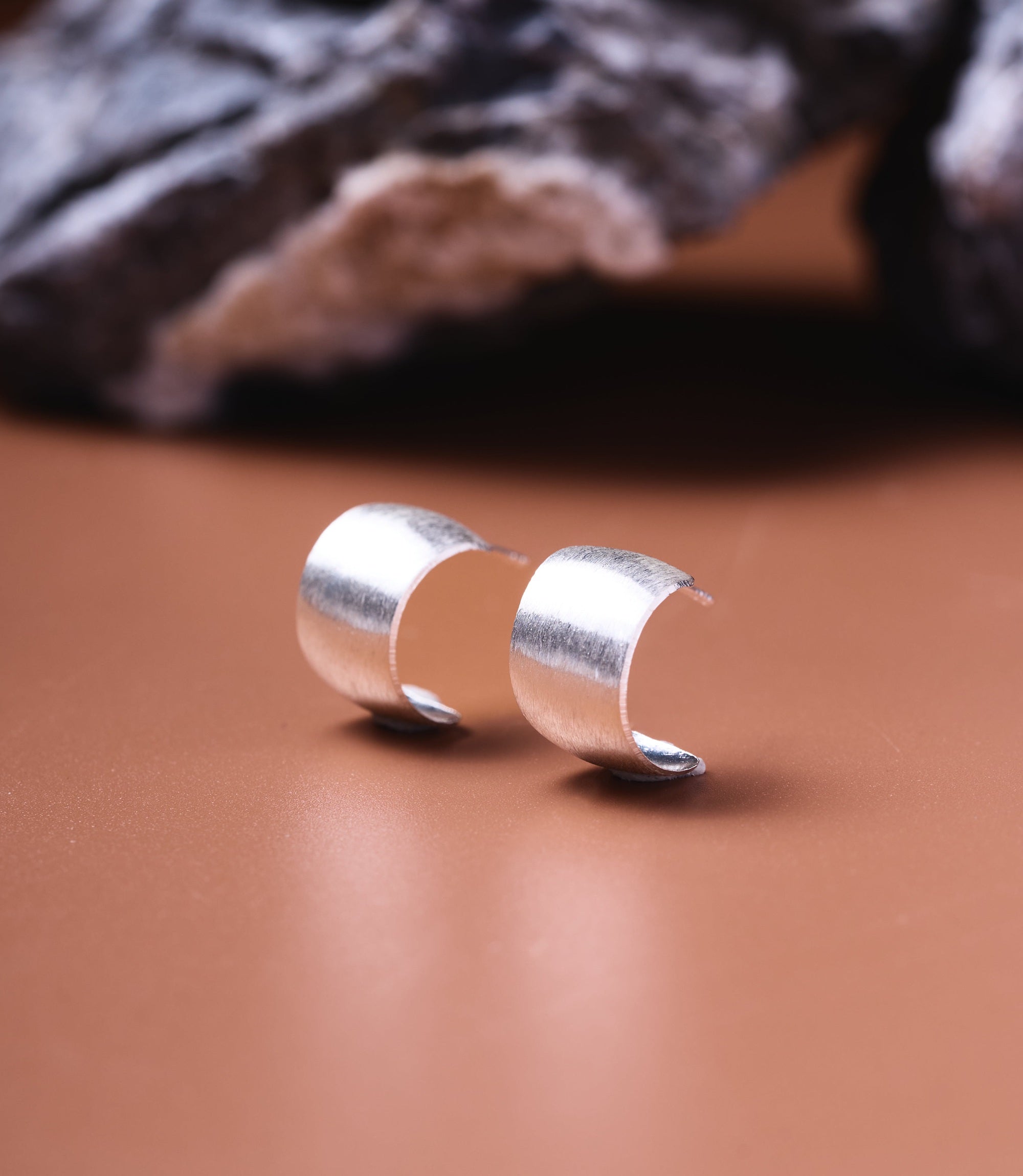 Cleo Sterling Silver Hoop Studs, wide brushed 925 sterling silver half-hoop stud earrings on a tan surface