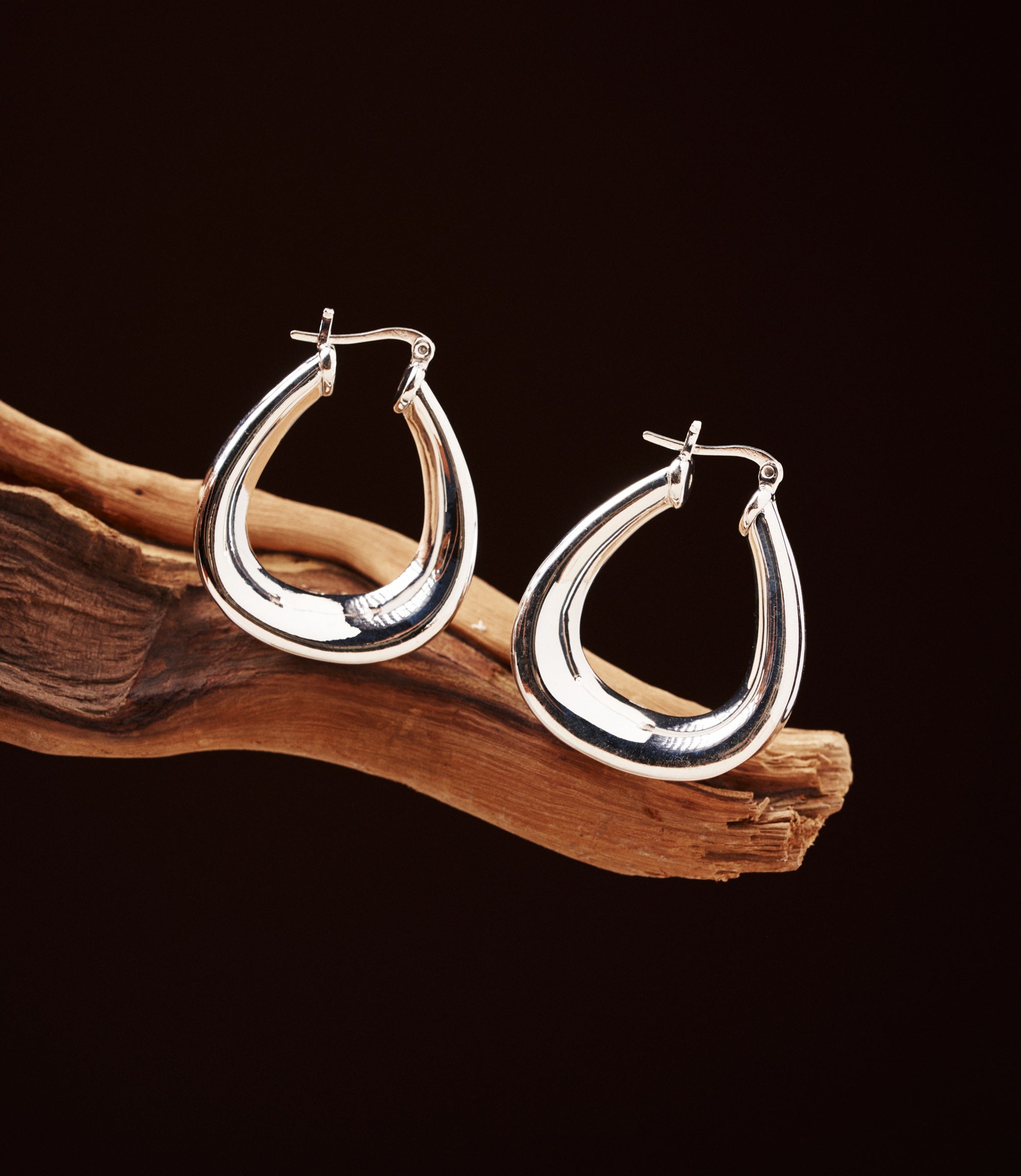 Romy Sterling Silver Hoops — polished 925 sterling silver teardrop hoop earrings resting on driftwood