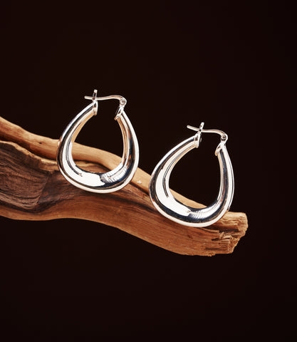 Romy Sterling Silver Hoops — polished 925 sterling silver teardrop hoop earrings resting on driftwood