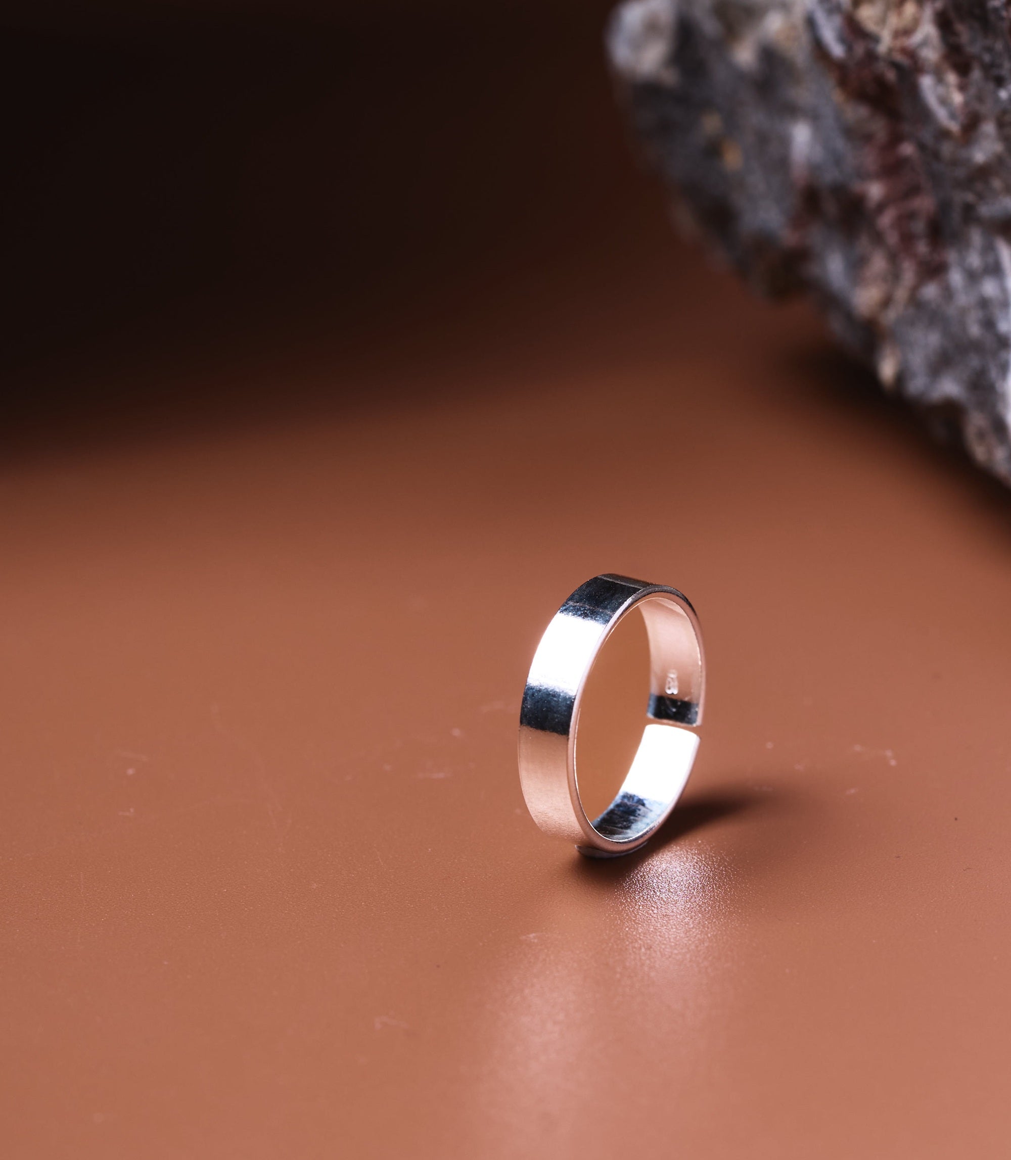 Zelia Sterling Silver 925 Toe Ring, a high-polish flat band ring on a warm brown surface