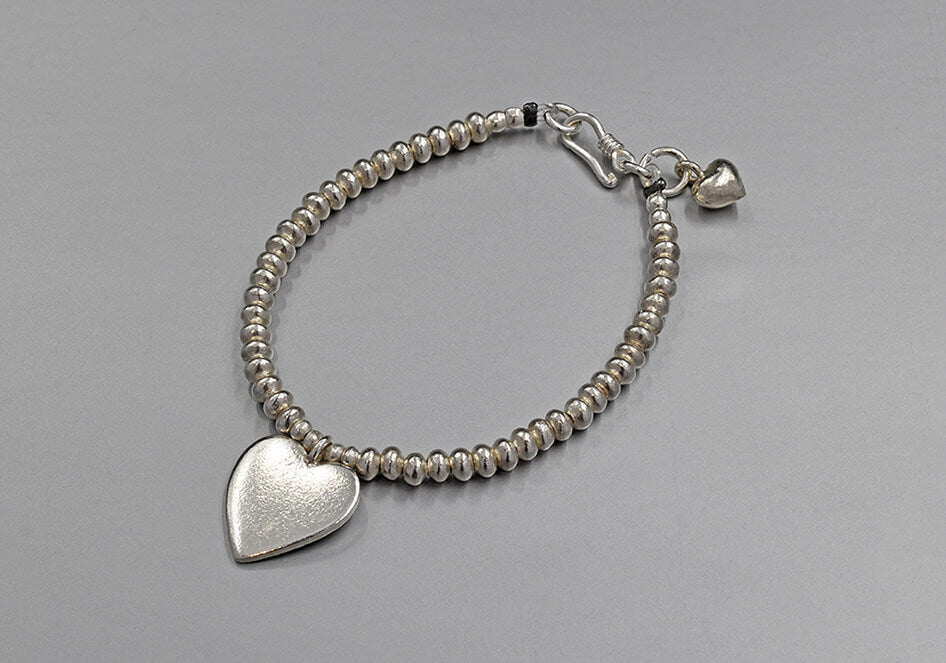 A cherished heart beaded bracelet with heart plate charm on light grey background.