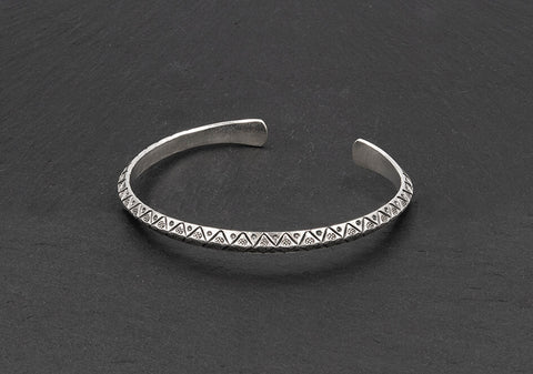 Hand-stamped silver cuff bangle from Hill to Street over a dark grey background