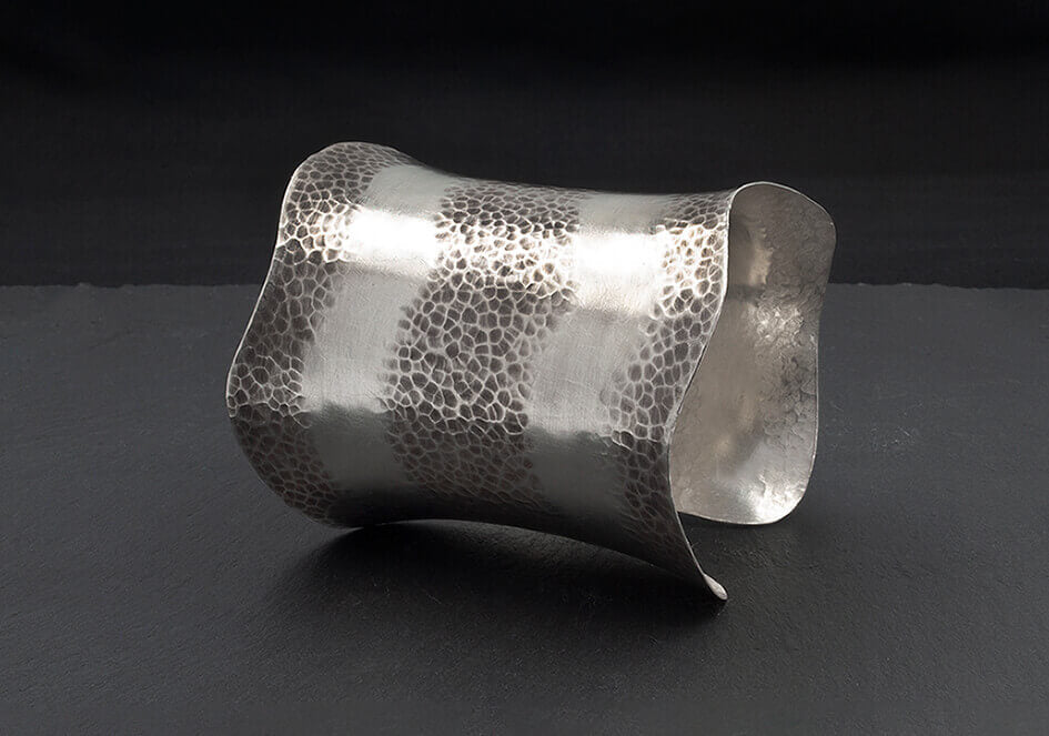 Long curved statement cuff bracelet over a black background