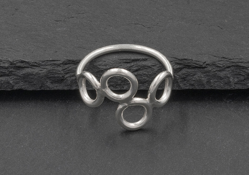 Angle view of a multi-circle silver ring from Hill to Street seating on a dark grey stone over black background