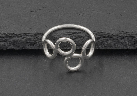 Angle view of a multi-circle silver ring from Hill to Street seating on a dark grey stone over black background