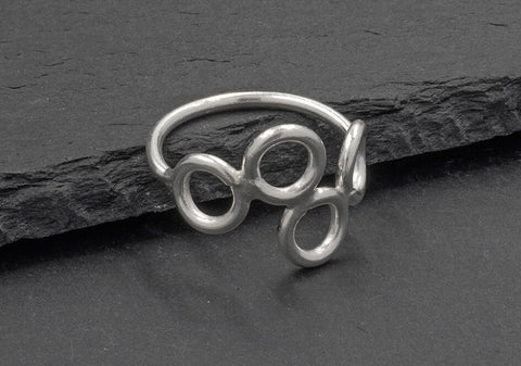 Side view of a multi-circle silver ring from Hill to Street seating on a dark grey stone over black background