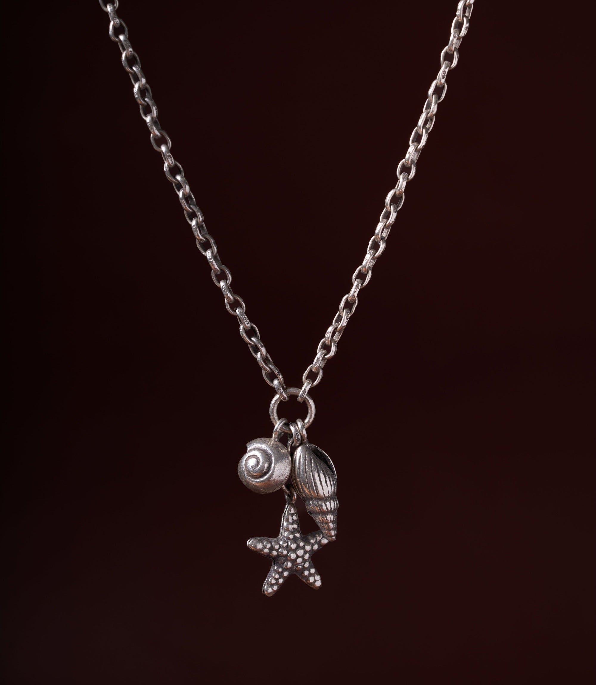The Cordelia Charm Necklace in pure silver featuring handcrafted seashell and starfish charms on a delicate silver chain.