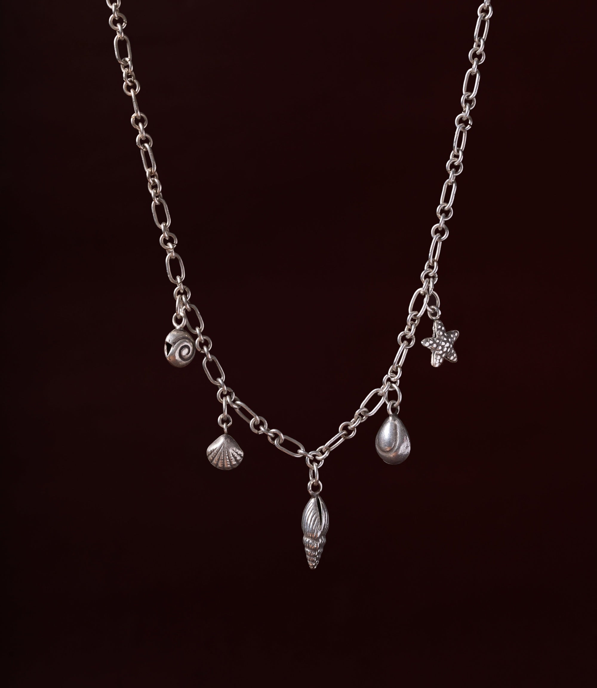 The Sienna Necklace in 925 sterling silver featuring ocean-inspired charms including a shell, starfish, spiral, and pearl detail.