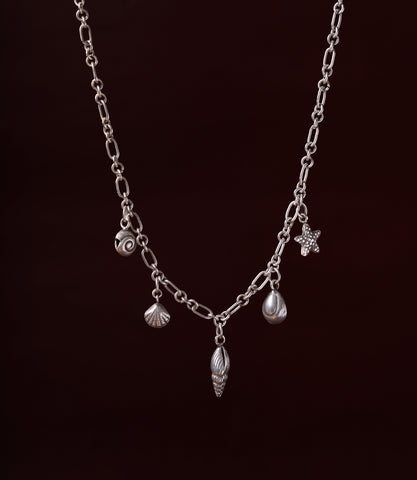 The Sienna Necklace in 925 sterling silver featuring ocean-inspired charms including a shell, starfish, spiral, and pearl detail.