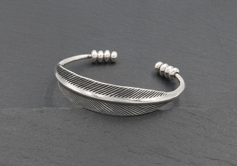 The Sylvie Bangle in pure silver featuring sculpted flat leaf details and polished silver beads on an open cuff design.