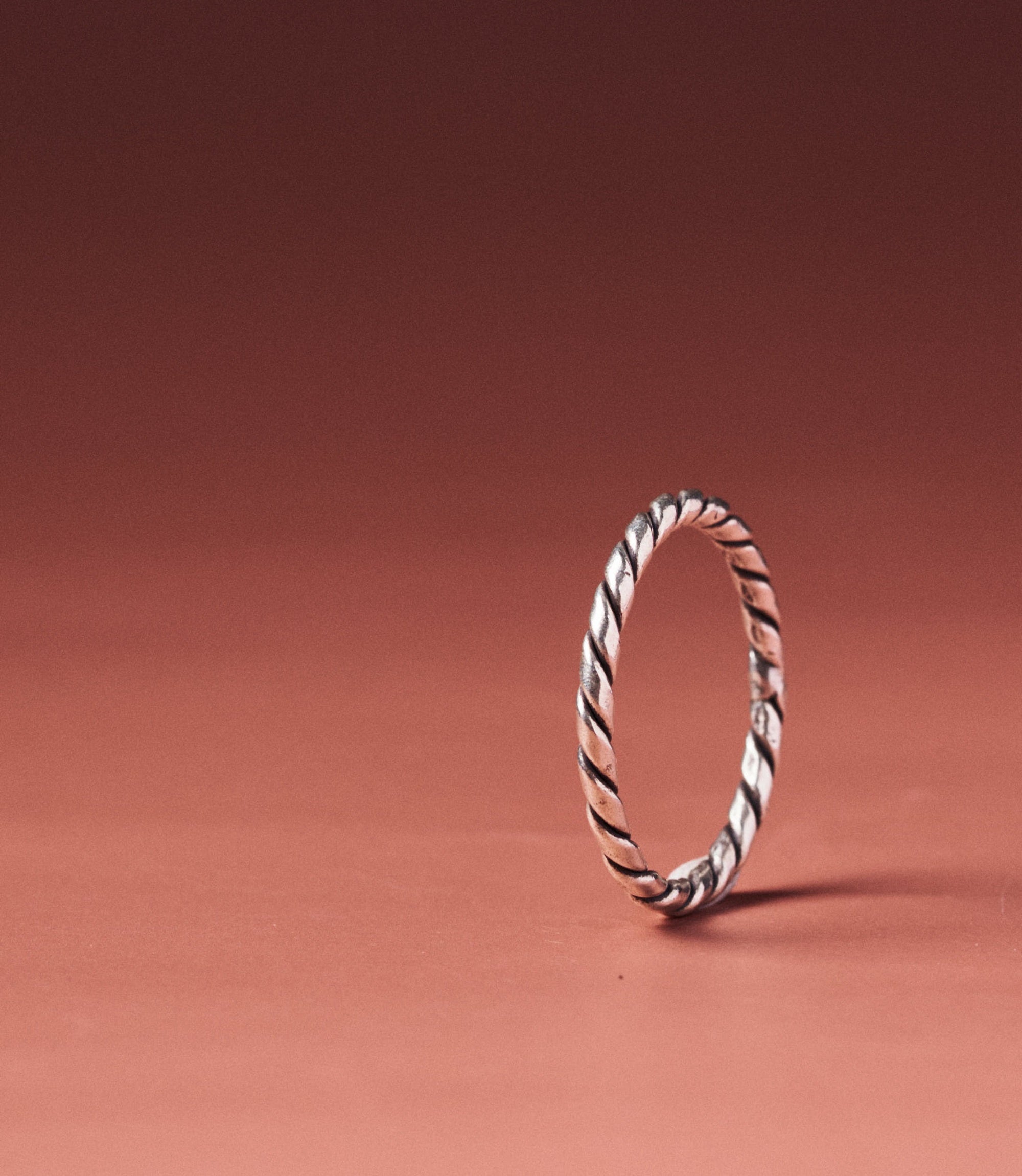 Alice Ring — handcrafted pure silver rope-twist band on a warm terracotta background