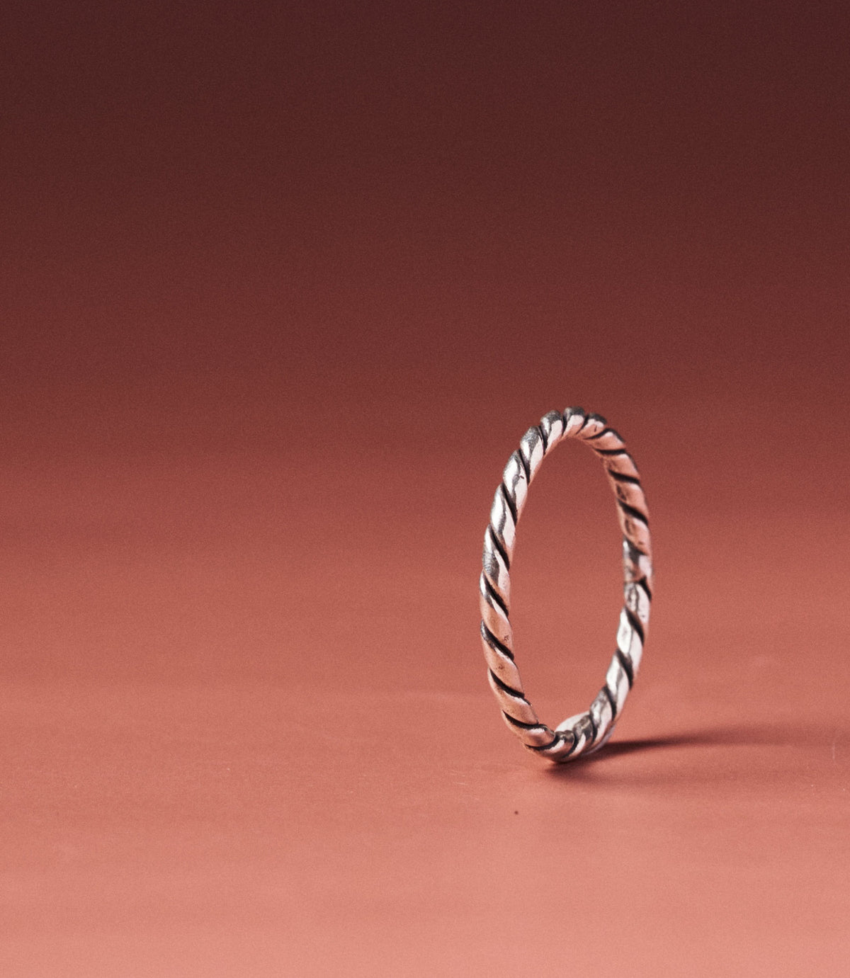 Alice Ring — handcrafted pure silver rope-twist band on a warm terracotta background
