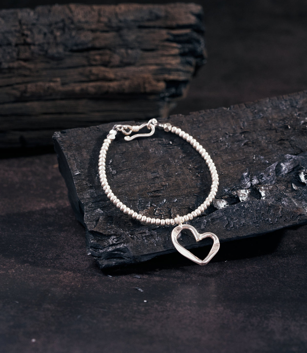 Sera Pure Silver Heart Charm Bracelet with open heart pendant and solid silver beads on dark charcoal surface