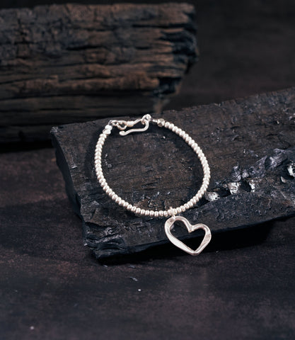 Sera Pure Silver Heart Charm Bracelet with open heart pendant and solid silver beads on dark charcoal surface