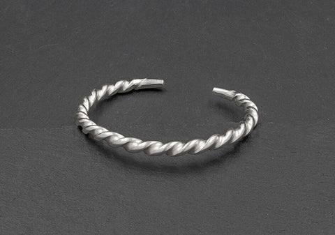 Shiny twisted bangle from Hill to Street over a dark grey textured background