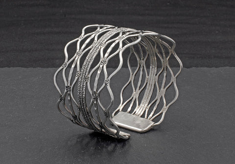 Stamped wavy silver wire cuff bracelet over a black textured background